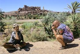 Image du Maroc Professionnelle de  Le paysage, formé par la kasbah Tifoultoute  qui se dresse majestueusement sur un éperon rocheux qui domine la vallée de l'oued Ouarzazate, attire les touristes qui prennent le temps de s'arrêter pour prendre une photo. Précisément à cet endroit un charmeur de serpent tenant une vipère avec sa main gauche tout en surveillant le mouvement du scorpion noir qu’il avait accroché à son cou avec sa main droite pose aux touristes contre un billet avec derrière lui comme décor celui qui avait servit pour de grand films comme Lawrence d’Arabie et Jésus de Nazareth à quelque kilomètres de la ville de Ouarzazate au sud du Maroc le Samedi 23 Août 1997. (Photo / Abdeljalil Bounhar)
